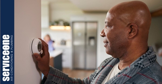 A man adjusting the temperature on a wall thermostat