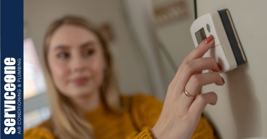A young adult woman pressing a button on a wall thermostat