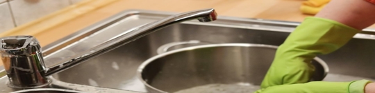 Hands with yellow gloves washing a pot in the sink.