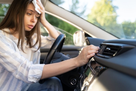 woman sweating in car, hands on air conditioning controls