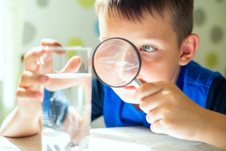 boy with a magnifying glass examining glass of tap water