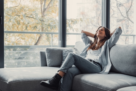 woman leaning back on a couch withi arms behind her head, relaxing, breathing easy