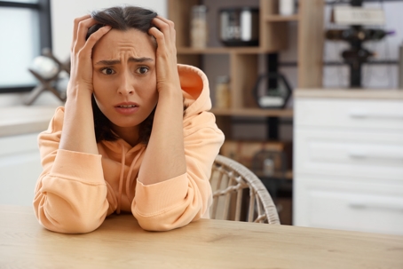 Dark-haired female homeowner holds hands against her head looking fearful