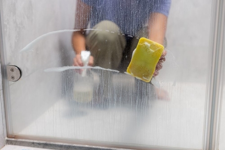 A hand cleaning a soap-scum covered shower door