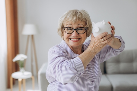 older woman smiling and holding up her piggy bank