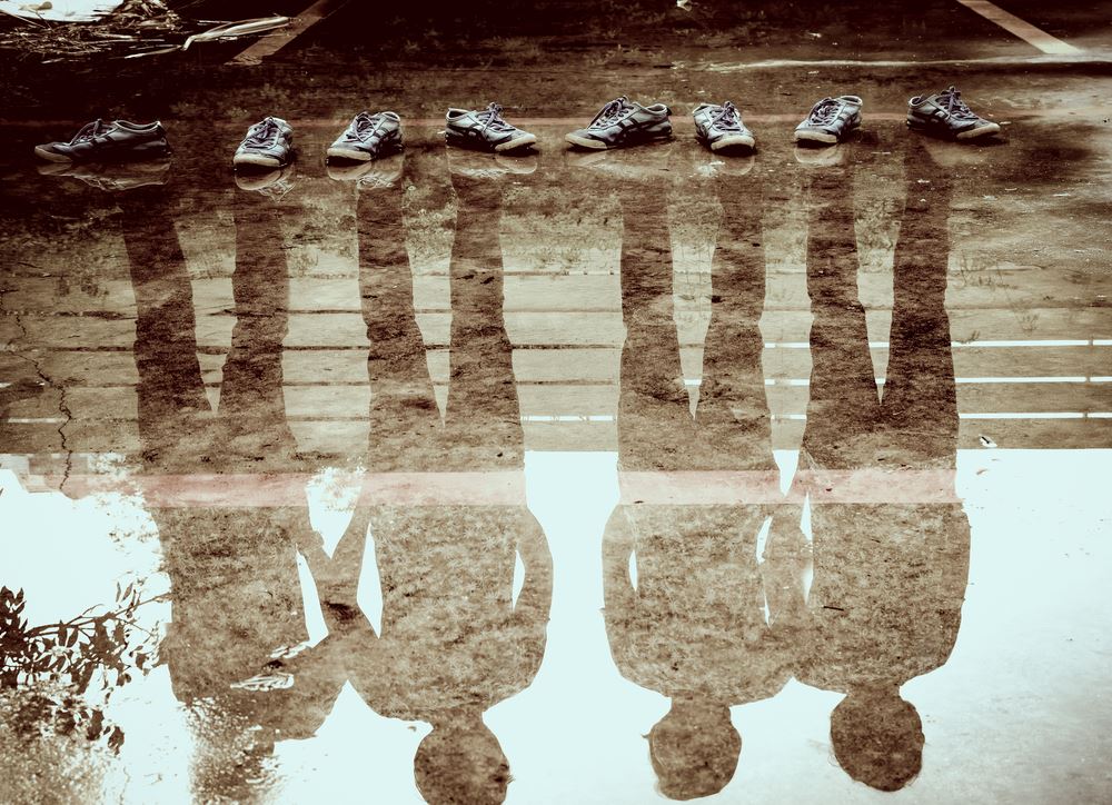 sepia toned pic of four men's reflections, shoes by the water