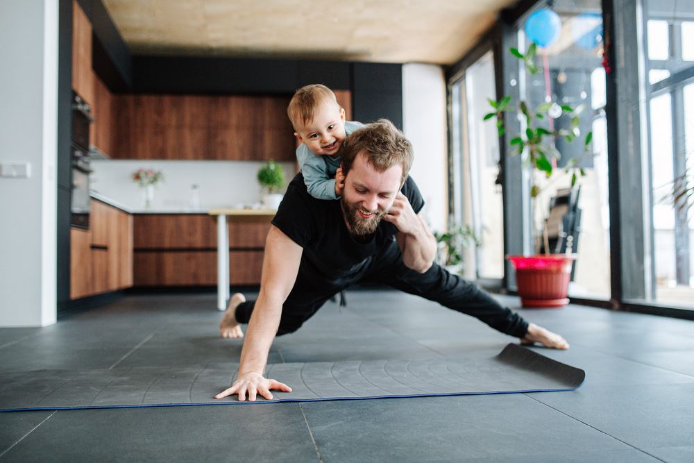 man doing push ups in the kitchen with a baby on his back