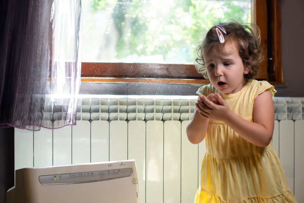 little girl coughing in front of window