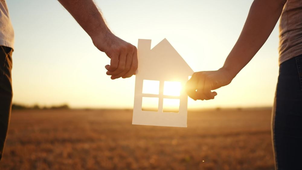 couple holding paper house with sunshine coming in the windows