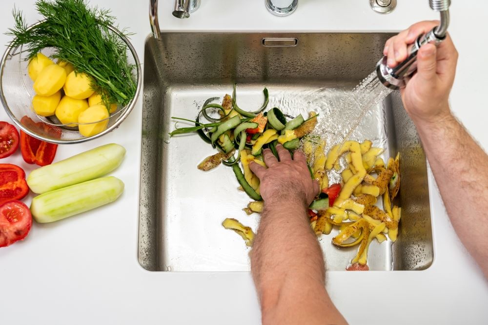 hand pushing peels down a garbage disposal