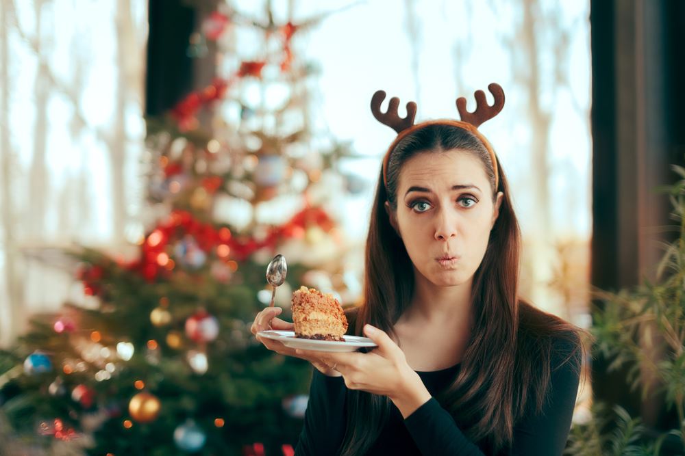 woman with reindeer antler headband and sad face in front of Christmas tree