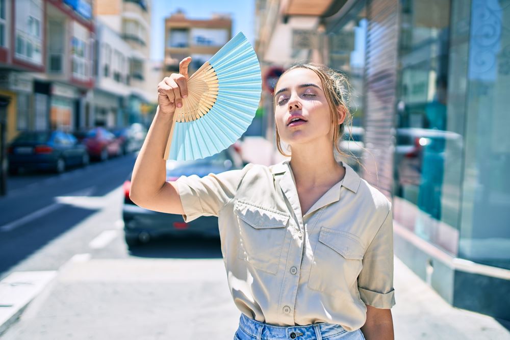 girl on city street fanning herself