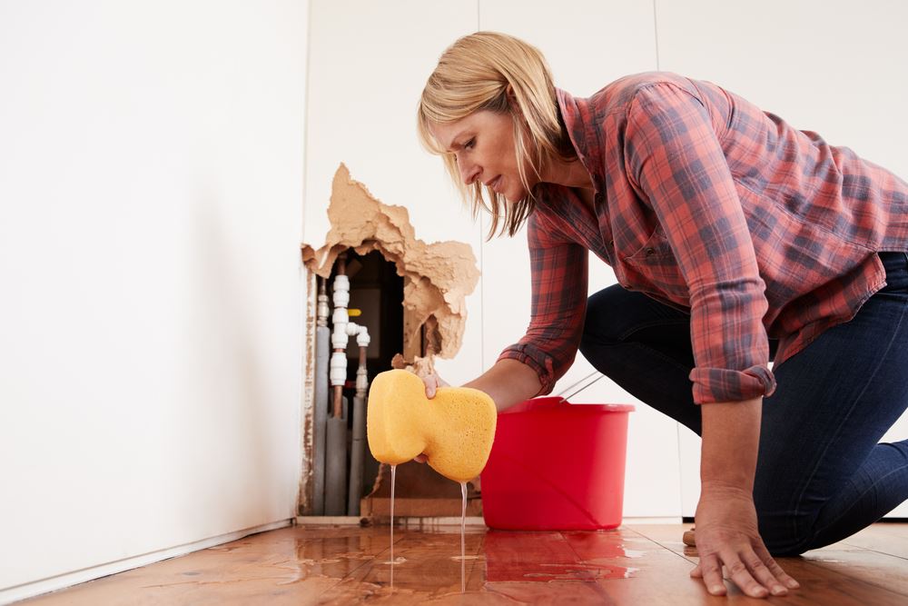 woman with sponge mopping water from floor in front of a hole in the wall