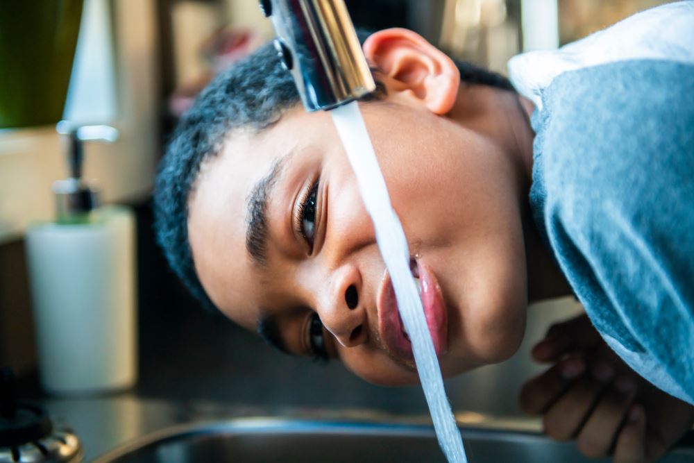 little boy drinking out of a running faucet