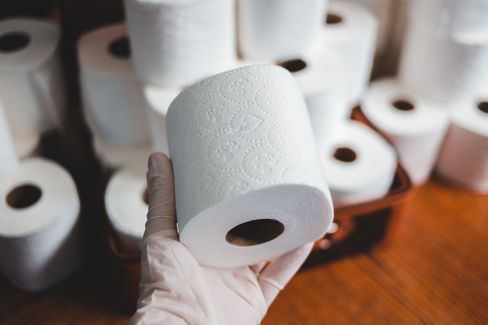 latex-gloved hand holding a roll of toilet paper 